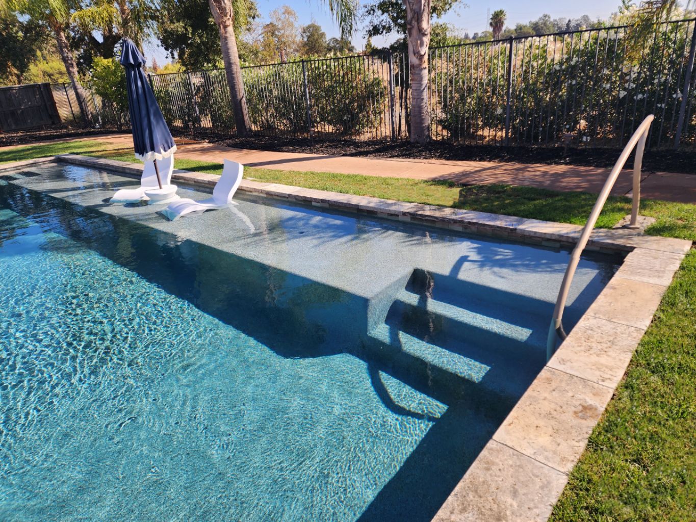 Rectangular shaped pool with a large Cabo shelf and a hand rail at entry steps and travertine stone coping.