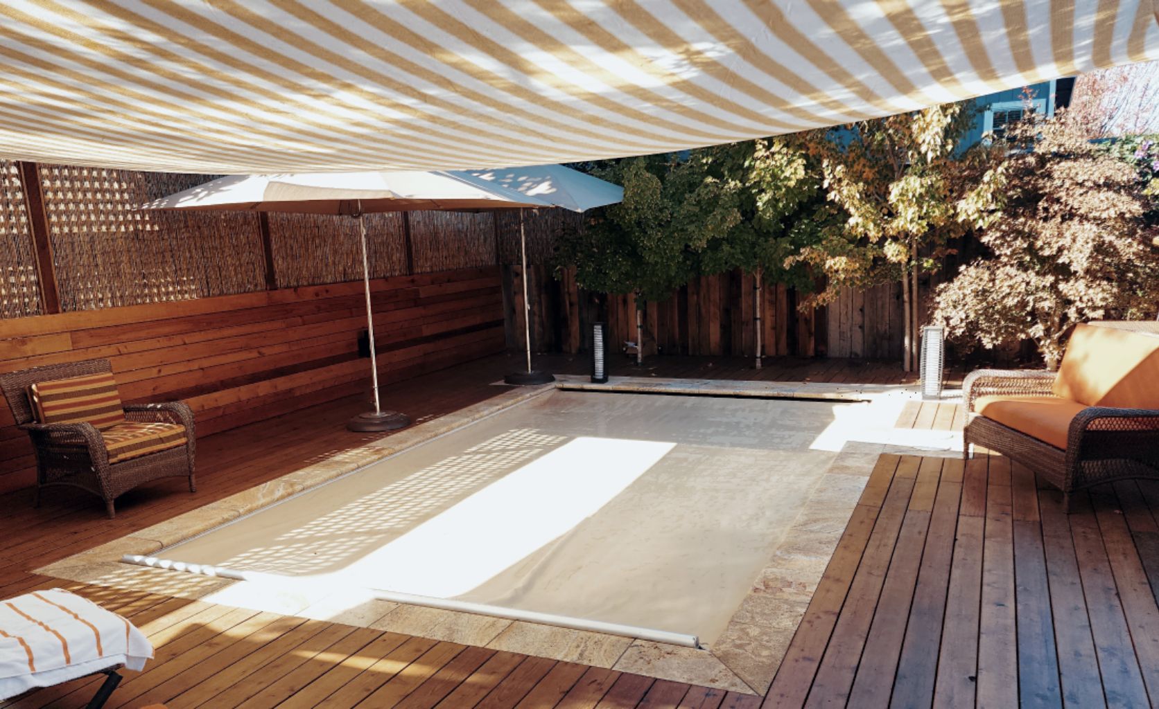 Small rectangular pool with a closed tan automatic pool cover and travertine stone coping surrounded by wood decking