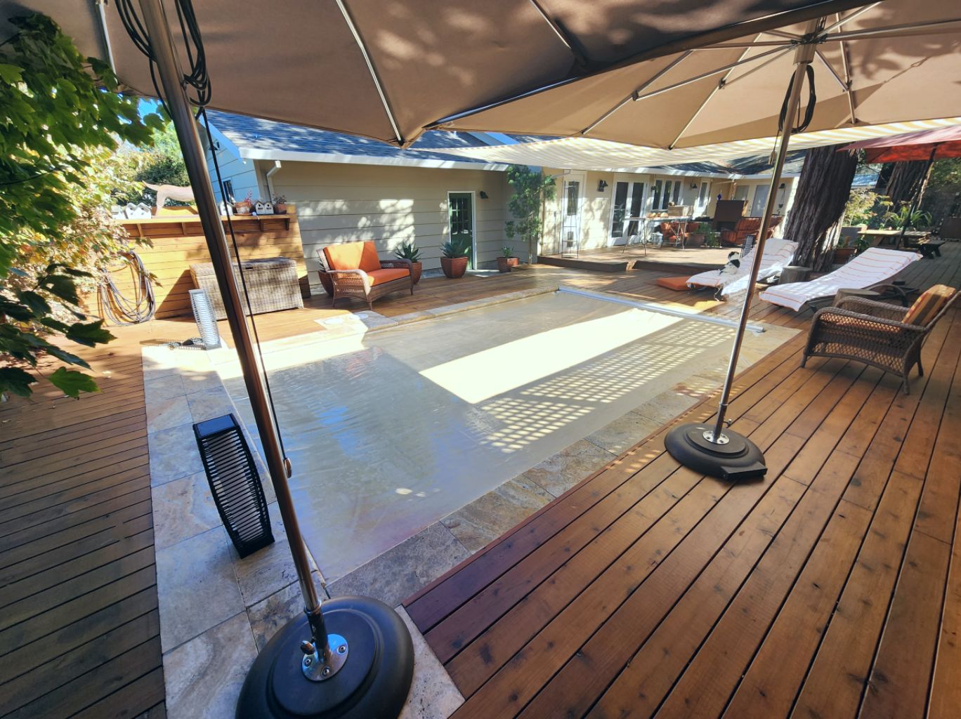 Small rectangular pool with a closed tan automatic pool cover and travertine stone coping surrounded by wood decking