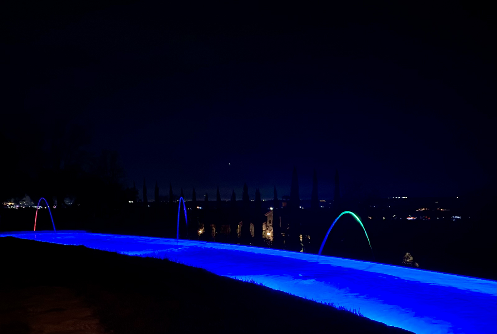 Large curved infinity edge pool with colored laminars at night.