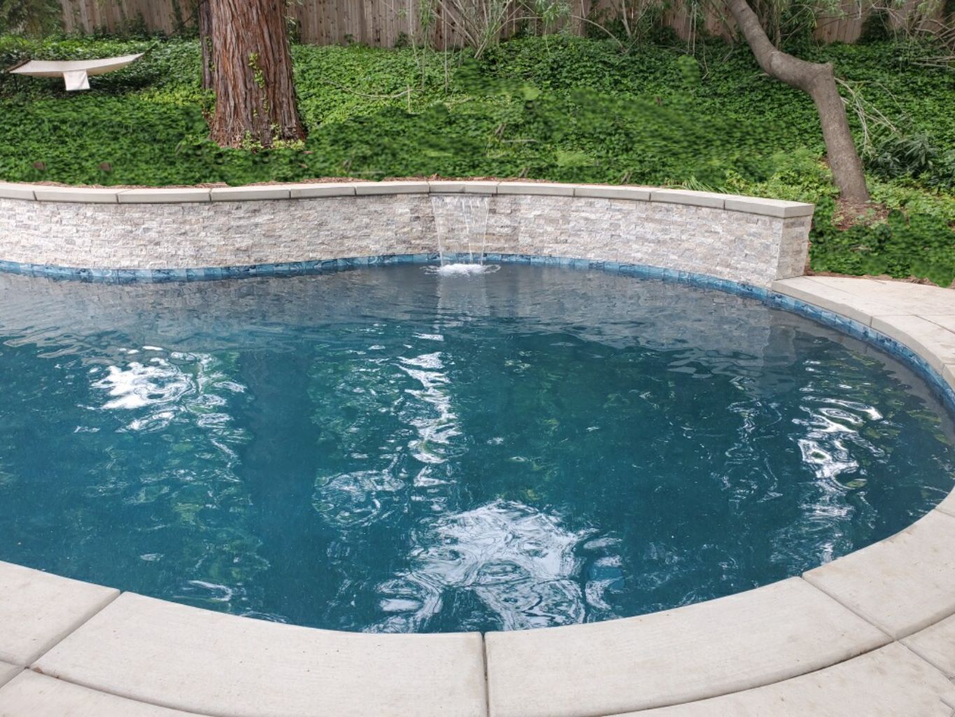 Freeform shaped pool with raised wall with ledgerstone and sheer descent water feature.