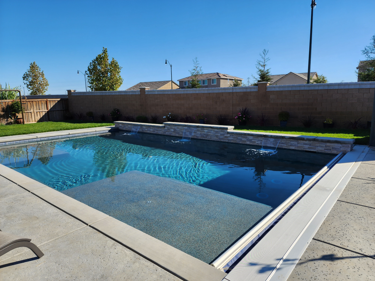 Rectangular shaped pool with raised tiered wall and three sheer descent water features, a Cabo shelf and an automatic pool cover with aluminum lid.
