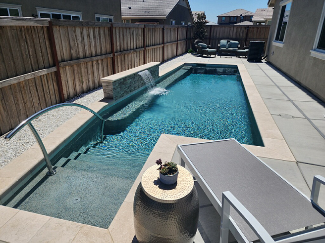 Small custom shaped pool with bumped out steps with a handrail and a raised wall with a sheer descent water feature with a seating bench underneath.