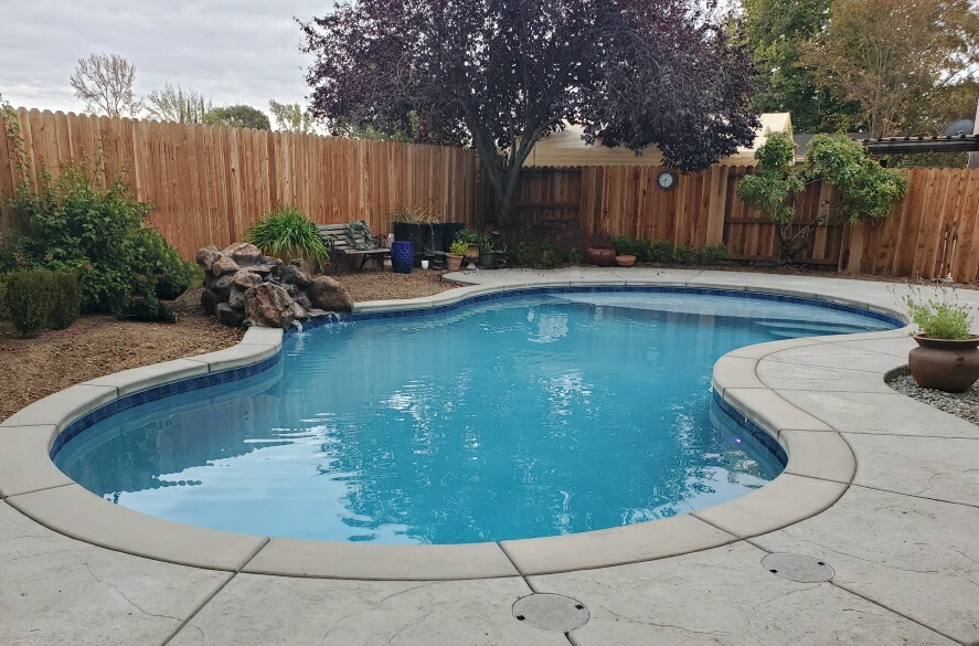 Freeform shaped pool with small rock waterfall and Cabo shelf