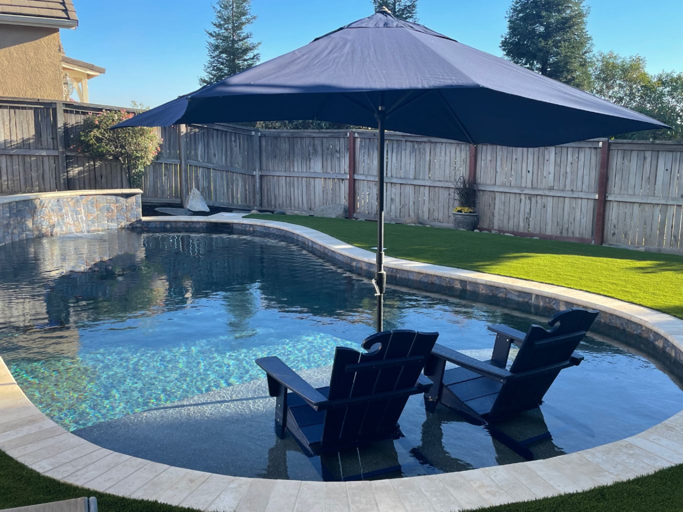 Freeform shaped pool with spa, sheer descent water feature, and Cabo shelf