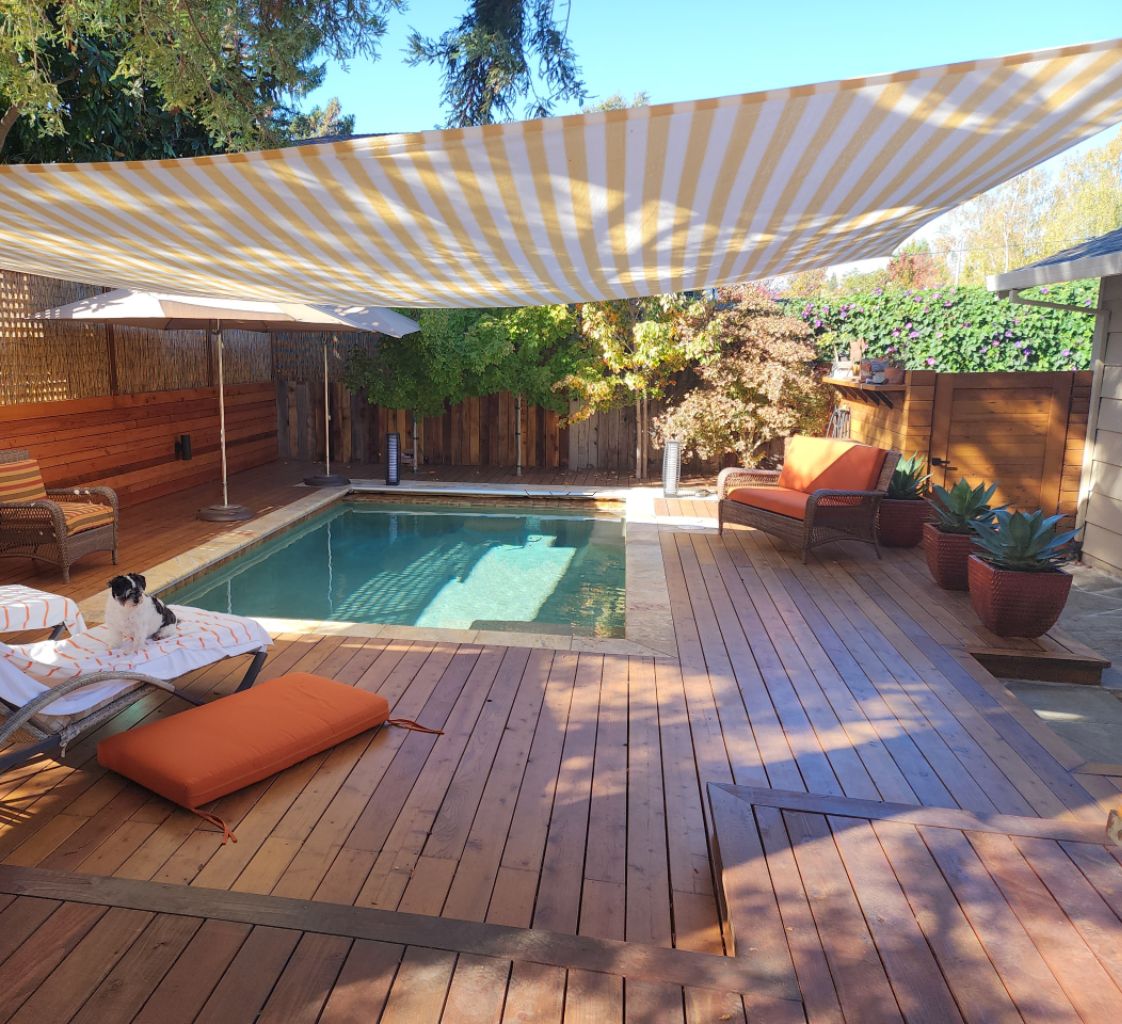 Small rectangular pool with an automatic pool cover and wood decking and a striped awning.