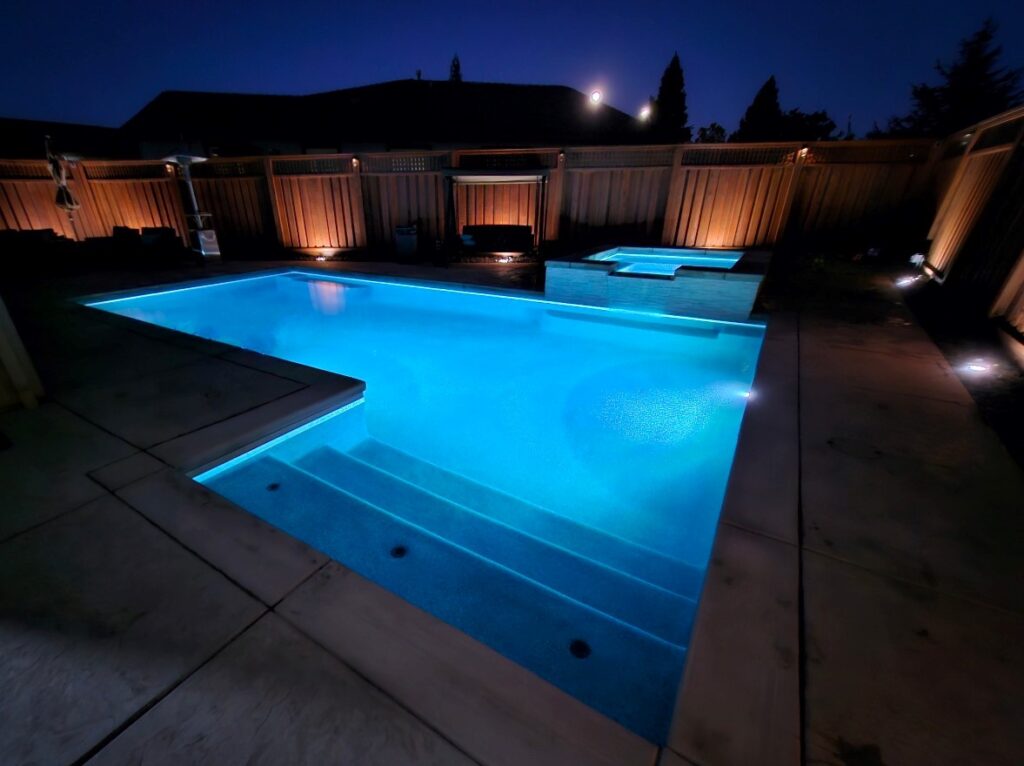Rectangular pool with raised spa and bumped-out Cabo shelf with entry steps at night