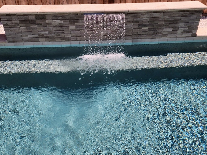 Sheer descent water wall feature on stone-textured pool wall